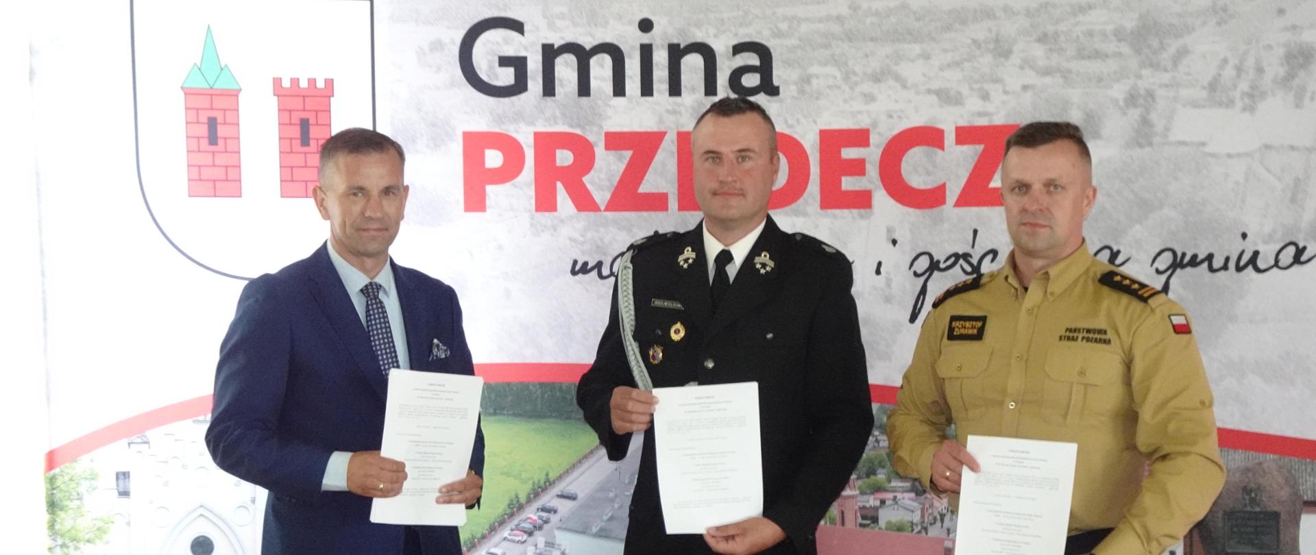 Zdjęcie przedstawia komendanta powiatowego PSP w Kole st. bryg. Krzysztofa Żurawika, burmistrza miasta i gminy Przedecz Jarosława Sobańskiego oraz prezesa OSP Przedecz druha Jarosława Boligłowę podczas podpisania trójstronnego porozumienia w sprawie włączenia jednostki OSP Przedecz do Krajowego Systemu Ratowniczo-Gaśniczego