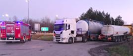 Na pierwszym planie (od lewej): samochód gaśniczo-ratowniczy Straży Pożarnej i dwa zestawy ciężarowe w trakcie przepompowywania benzyny z nieszczelnej cysterny. 