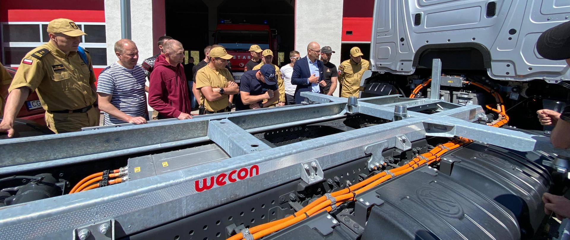 Tylna część samochodu ciężarowego, przy której odbywa się szkolenie dla zgromadzonych wokół strażaków.