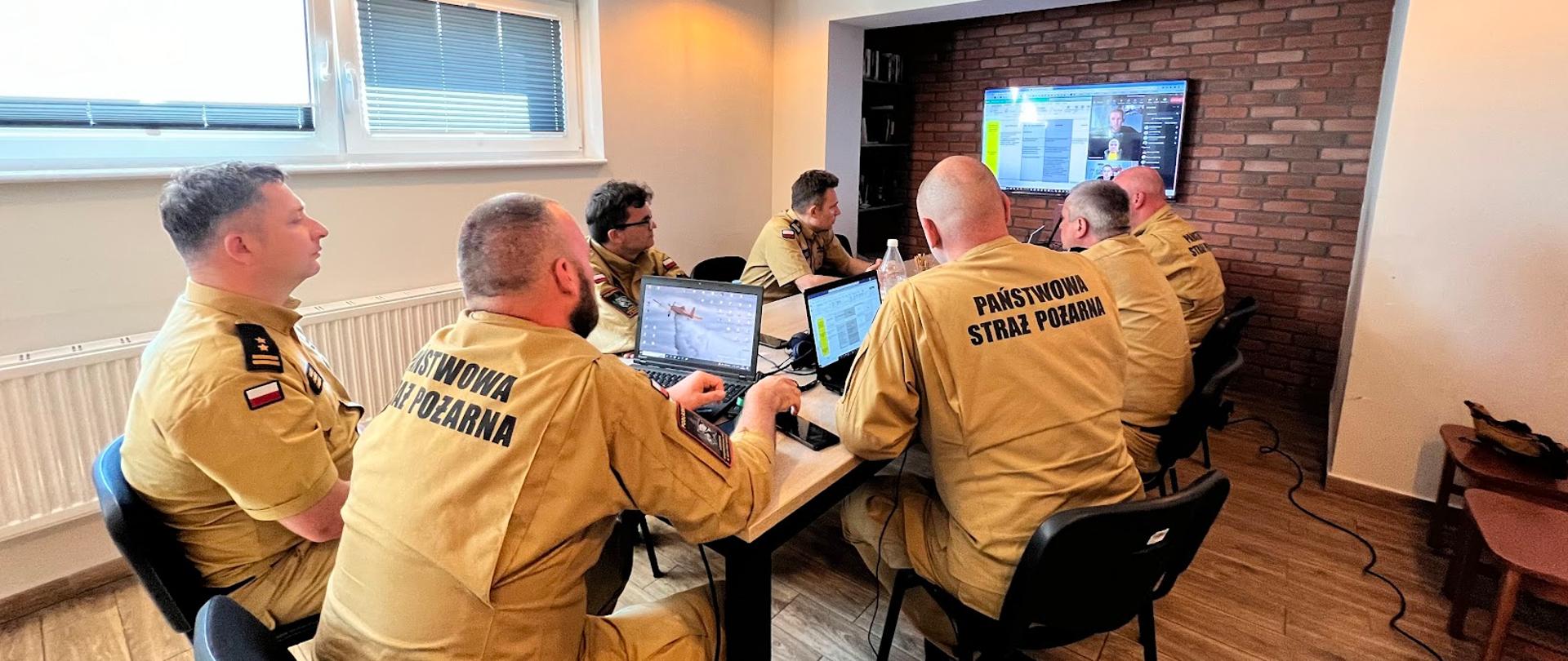 siedmiu funkcjonariuszy w piaskowych mundurach siedzących przy wspólnym stole