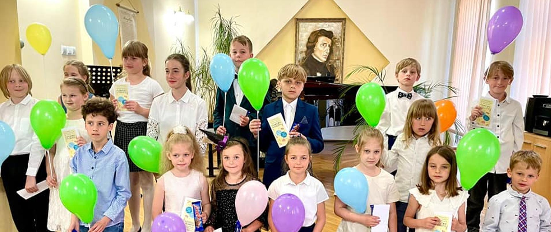 grupa dzieci uczestniczących w koncercie pt. "Muzyczne debiuty" uczniów klas pierwszych - 31 maja 2023 pozujący do zdjęcia grupowego wraz z balonami