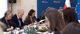 Grupa osób siedzi przy stole konferencyjnym, na pierwszym planie widać ministra Zajączkowskiego i Dyrektorkę Piątkowską, z tyłu widać flagę Polski i Unii Europejskiej