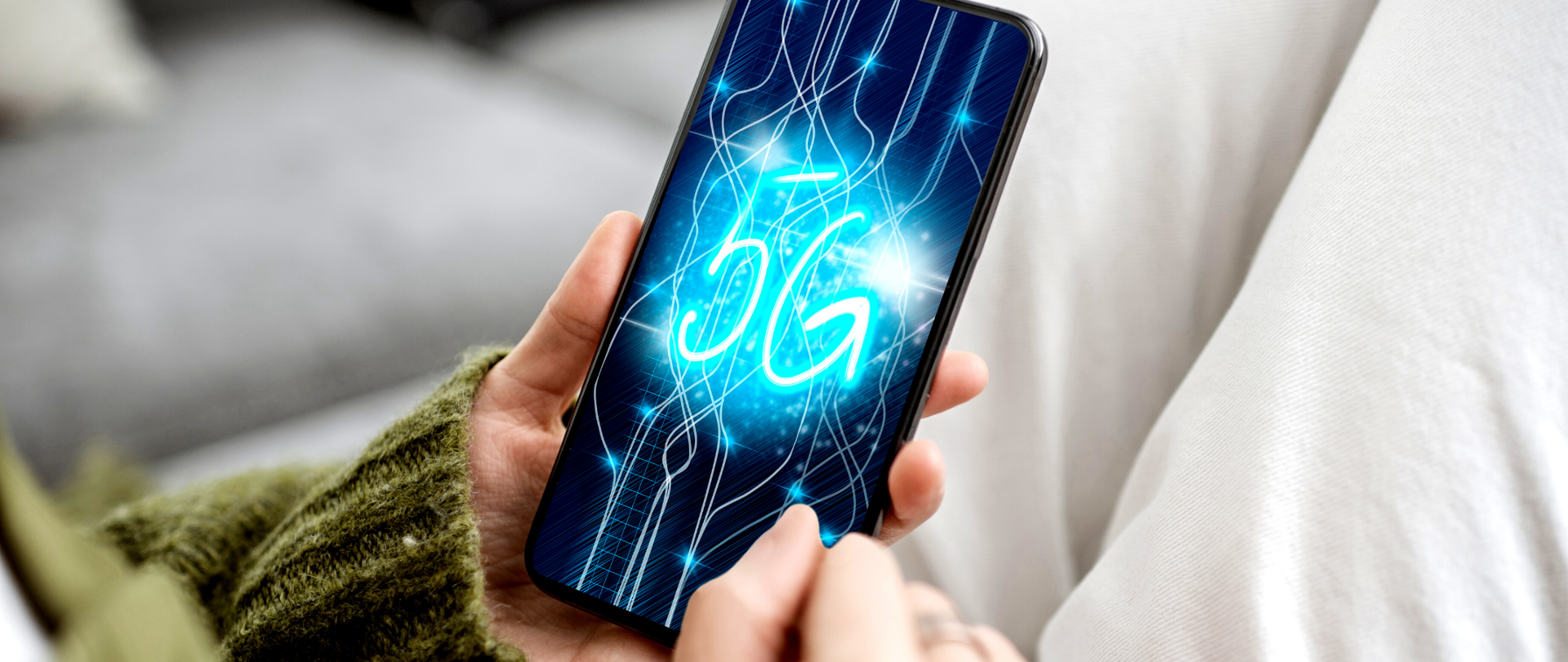 Dłonie trzymające telefon komórkowy, na ekranie napis: 5G
