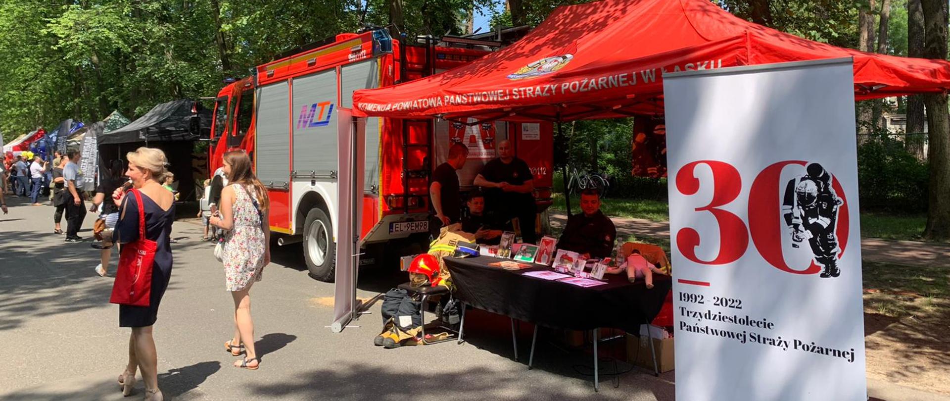 Zdjęcie przedstawia strażaków na stoisku PSP podczas pikniku rodzinnego w Łasku - Kolumnie
