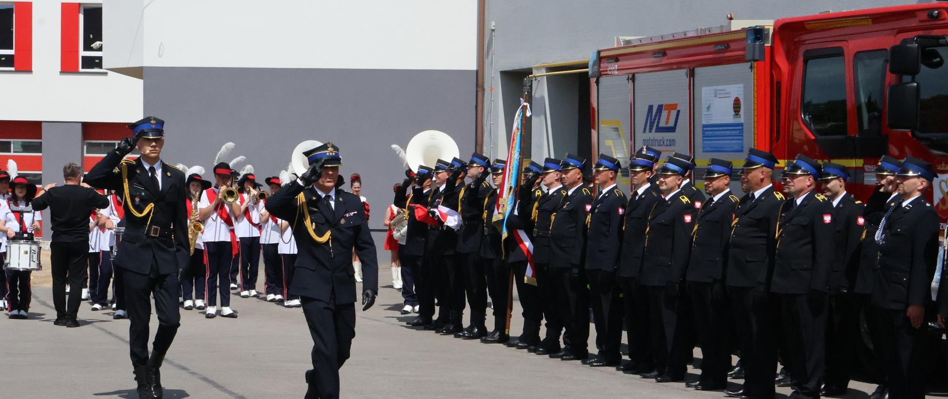 Powiatowy Dzień Strażaka w Zwoleniu oraz uroczyste przekazanie samochodu ratowniczo – gaśniczego dla OSP Zielonka Nowa. Dwóch strażaków maszeruje przed pododdziałem strażaków. 