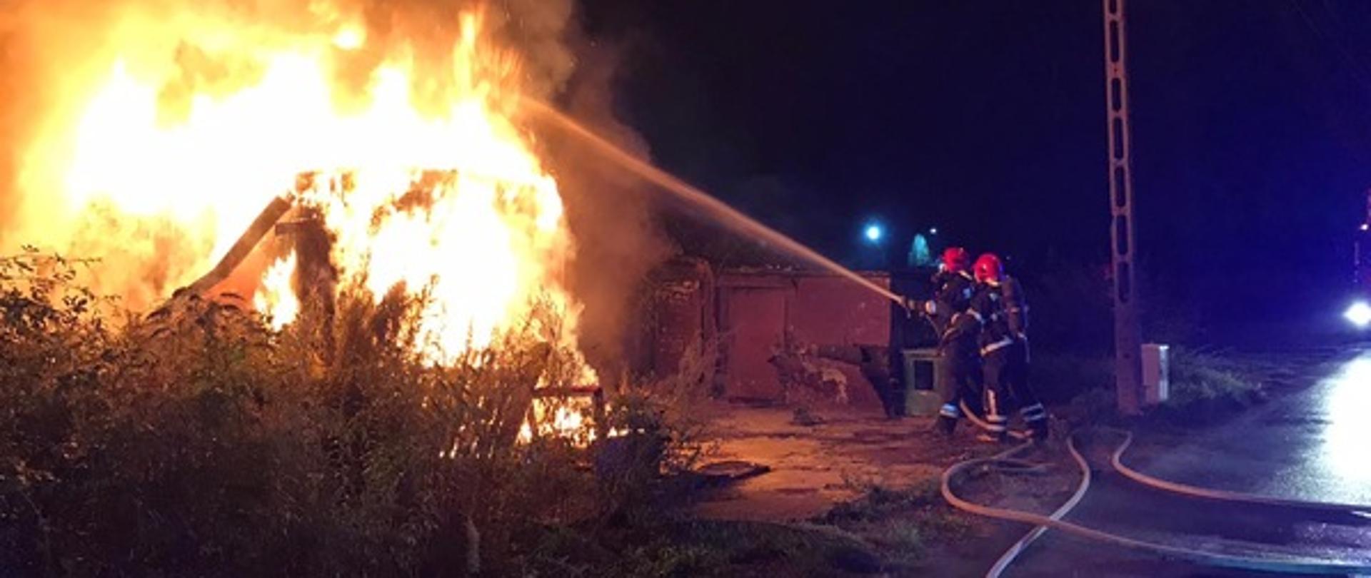 Pora nocna. Przednia część budynku cała w ogniu. Płomienie sięgające 6 metrów. Rota strażaków podaje prąd wody na palący się budynek. Obaj ubraniu w sprzęt ochrony układu oddechowego. Rozwinięte dwie linie gaśnicze.