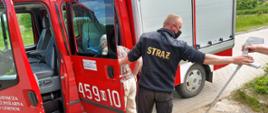 Zdjęcie przedstawia strażaka OSP w Górnem pomagającego kobiecie wejść do pojazdu pożarniczego w celu transportu do punktu szczepień