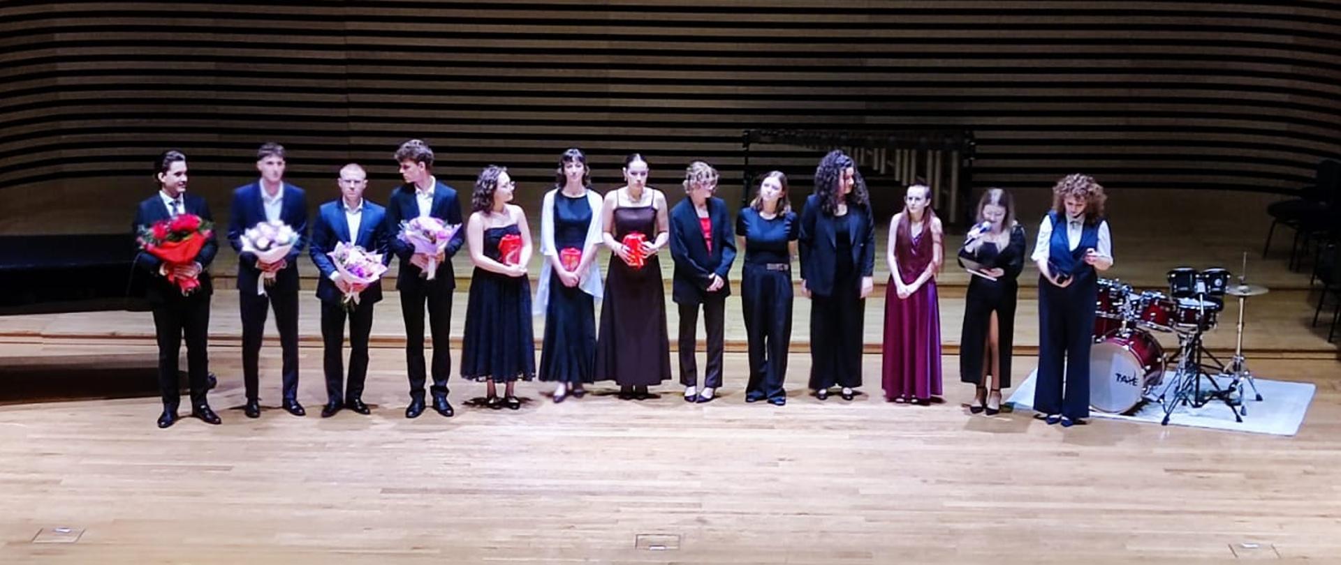 Na scenie stoją w rzędzie czterech chłopaków i dziewięć dziewczyn.