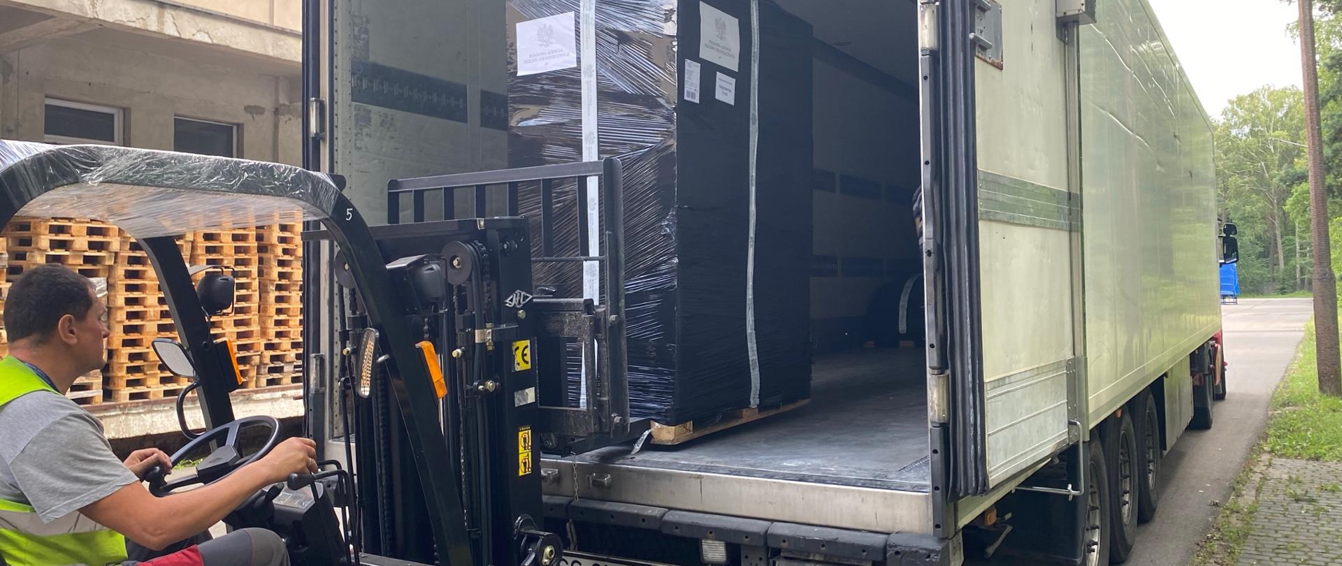 Mężczyzna wkłada wielką paczkę za pomocą wózka widłowego do ciężarówki