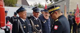 Na zdjęciu widać funkcjonariuszy przed remizą OSP Janów podczas uroczystego przekazania pojazdu. Na pierwszym planie funkcjonariusze Państwowej i Ochotniczej Straży Pożarnej. Generał PSP Śląski Komendant Wojewódzki Państwowej Straży Pożarnej nadbryg Jacek Kleszczewski podczas wręczania pamiątkowej statuetki. 