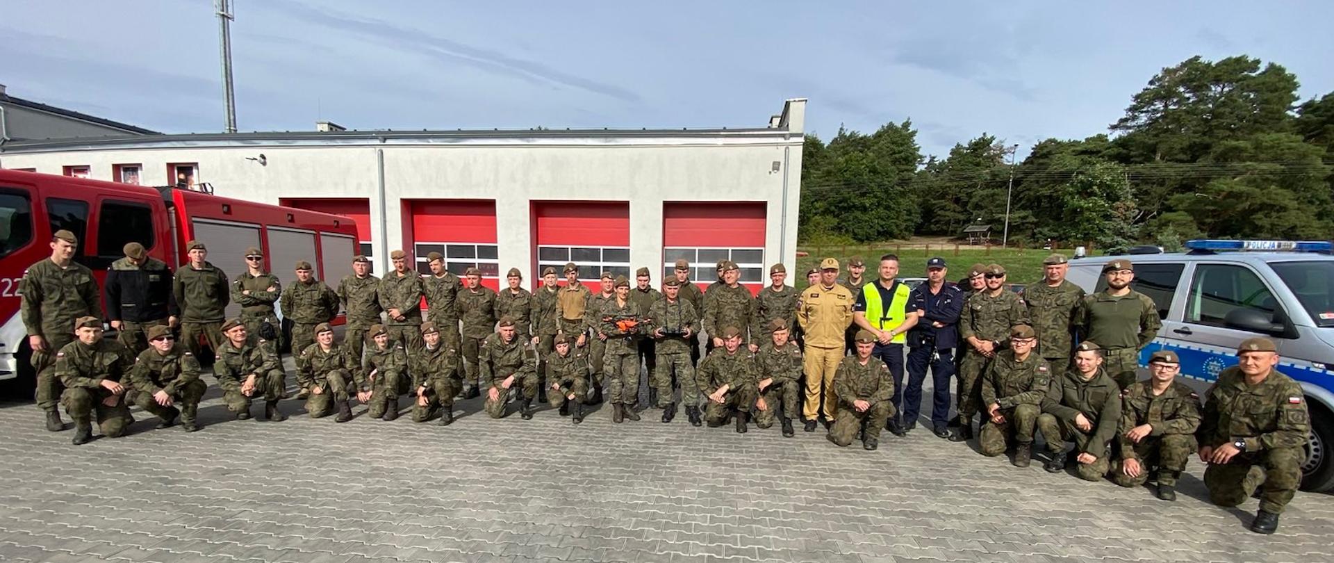Pamiątkowe zdjęcie żołnierzy w mundurach moro ustawieni półkolem na utwardzonym placu.
