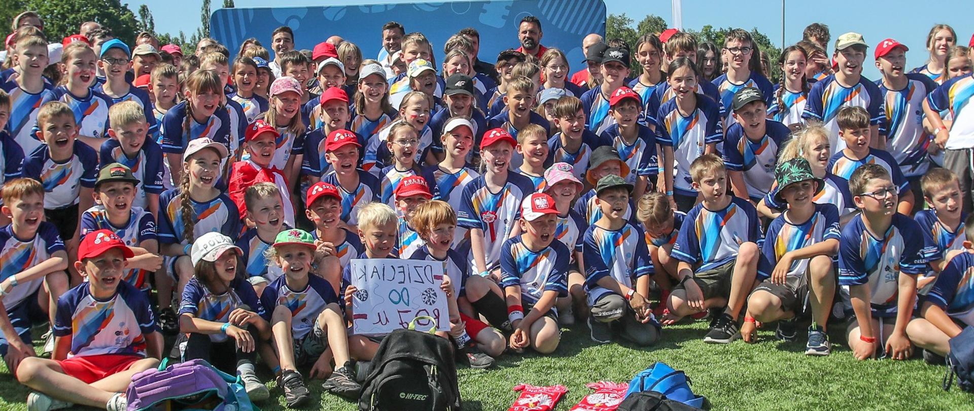 Grupa dzieci z Programu Szkolny Klub Sportowy pozuje do zdjęcia z ministrem Kamilem Bortniczukiem i gośćmi Dnia Dziecka, który odbył się w ośrodku Legia Training Center w Książenicach