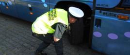Inspektor transportu drogowego kontroluje stan bieżnika opon autokaru podstawionego w miejsce wyjazdu na obóz harcerski.