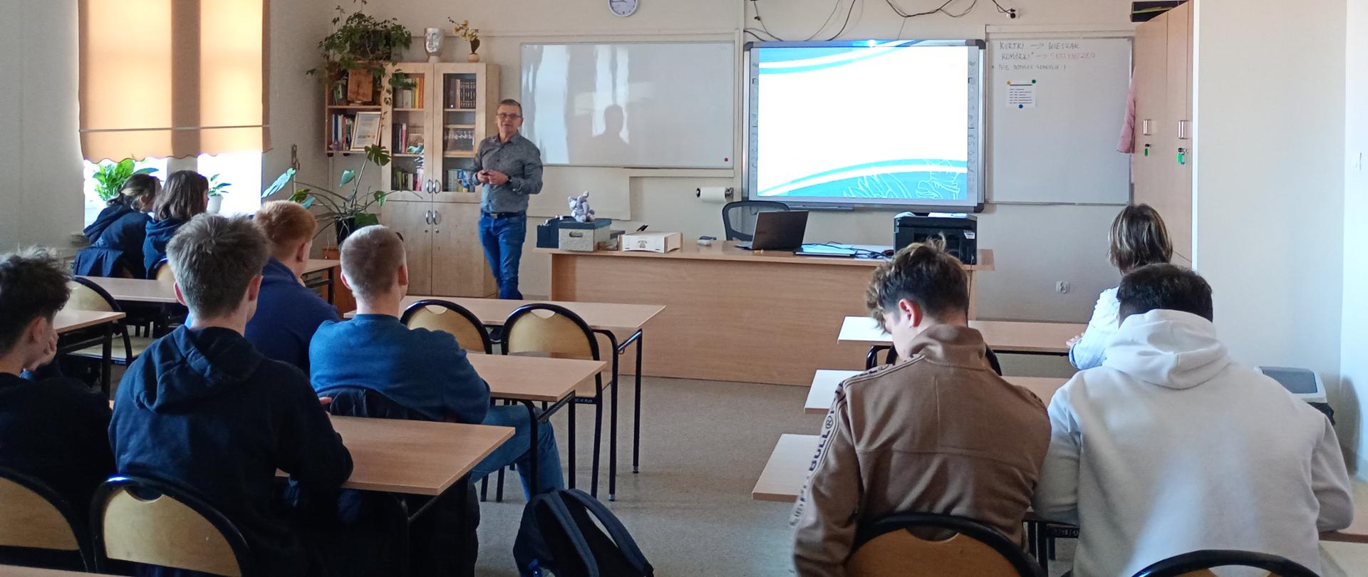 Uczestnicy siedzący na sali lekcyjnej z wykładowcą.