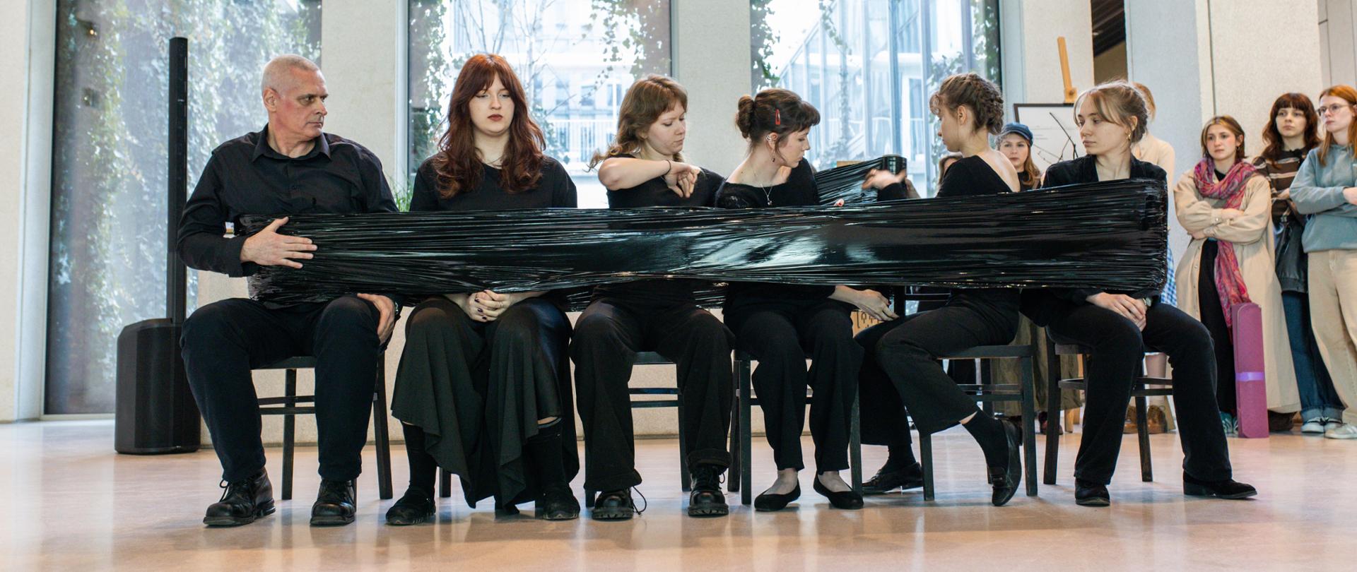 Uczniowie siedzący na krzesłach we wnętrzu Galerii Wena