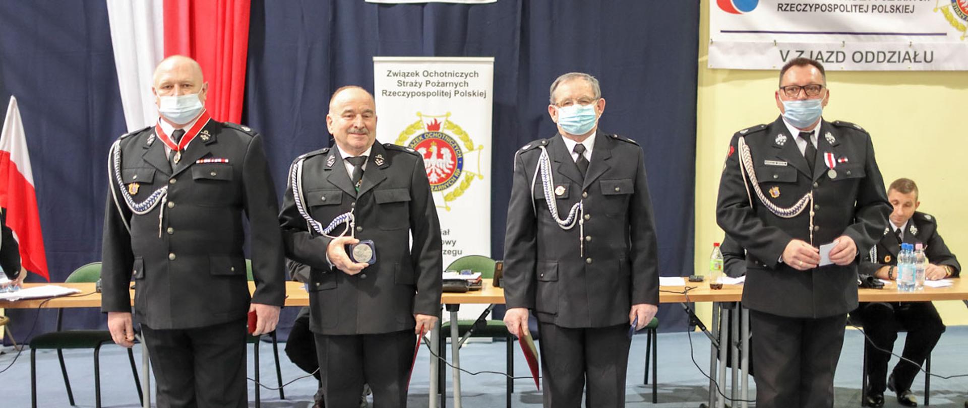 Strażacy stojący w rzędzie, za nimi stół, na ścianie godło RP i logo ZOSP RP.