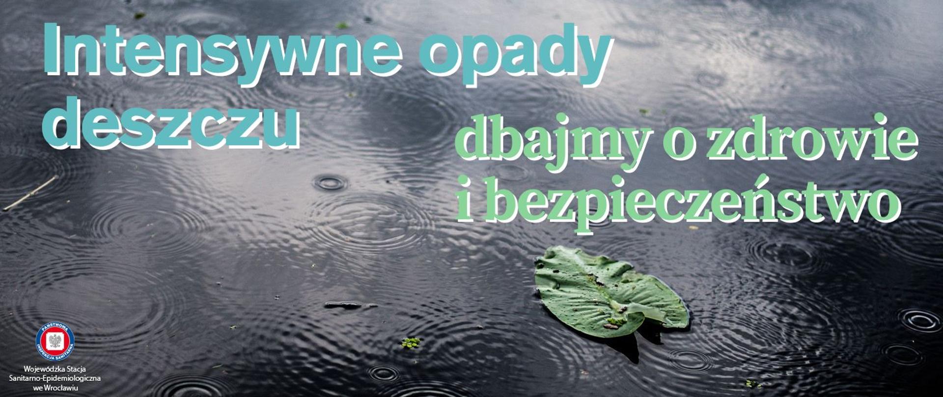 Asfaltowa powierzchnia w czasie deszczu. Widać rozpryski kropel wody oraz zielony liść