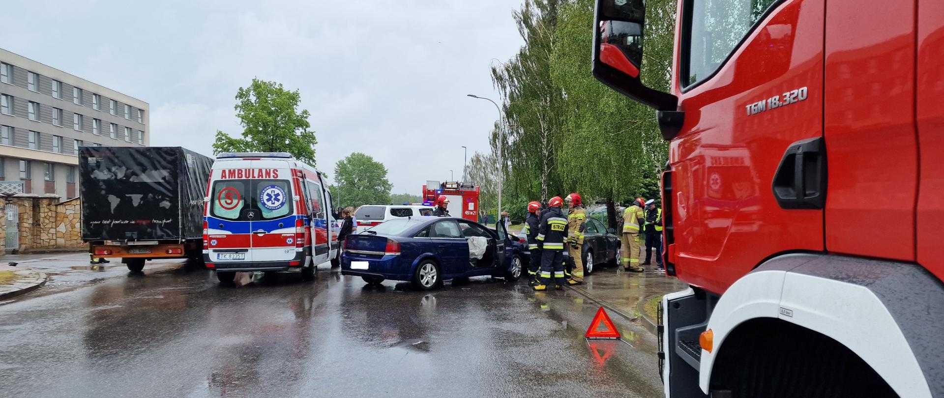 Na pierwszym planie samochody osobowe biorące udział w zdarzeniu drogowym, funkcjonariusze PSP w pełnych ubraniach bojowych. W tle samochody bojowe PSP oraz ZRM.