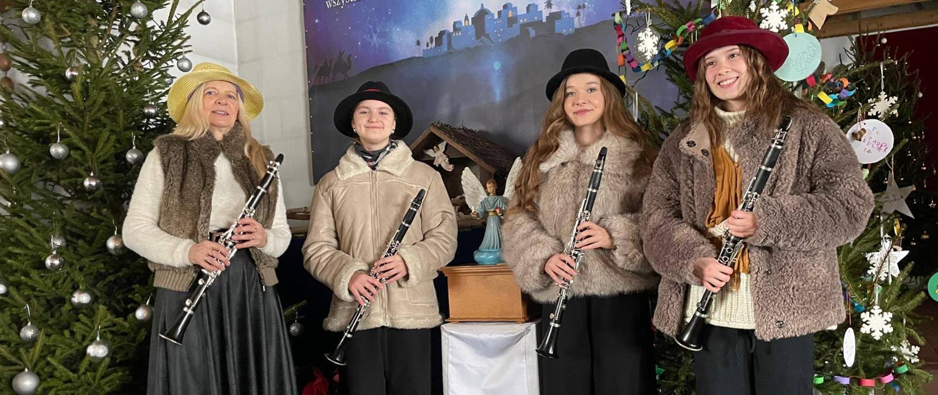 Uczennice z trio klarnetowego wraz z nauczycielką Anną Łysko pozują w strojach pastuszka w kościele trzymając klarnety.