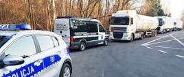 Policyjny patrol w miejscu kontroli podlaskiej Inspekcji Transportu Drogowego. Na pierwszym planie radiowóz Policji, dalej furgon ITD i zatrzymane ciężarówki.