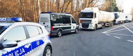 Policyjny patrol w miejscu kontroli podlaskiej Inspekcji Transportu Drogowego. Na pierwszym planie radiowóz Policji, dalej furgon ITD i zatrzymane ciężarówki.