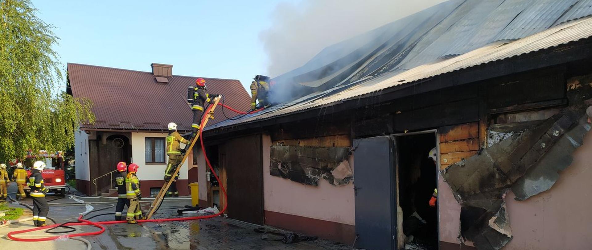 Strażacy z drabiny przystawnej gaszą pożar budynku gospodarczego,. 