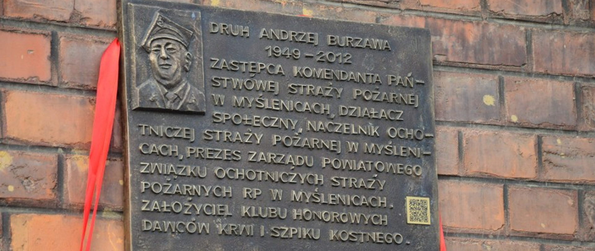 Zdjęcie przedstawia pamiątkową tablicę znajdującą się na budynku strażnicy OSP Myślenice Śródmieście. Przedstawia ona postać dh Andrzeja Burzawy, który został patronem ronda w centrum Myślenic.