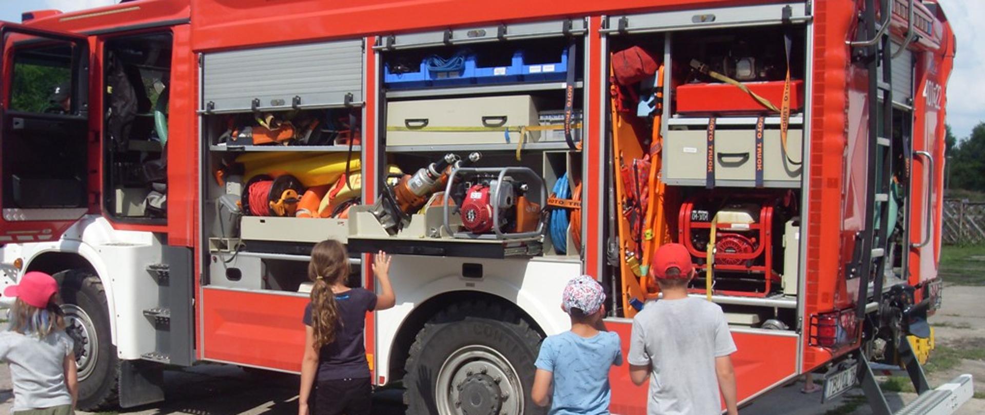 Zdjęcie przedstawia grupę uczestników prelekcji oglądających wyposażenie samochodu pożarniczego