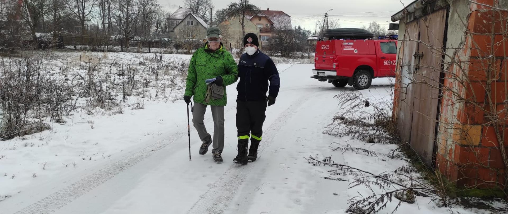 na zdjęciu strażak pomaga starszemu mężczyźnie w dojściu do punktu szczepień