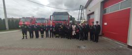 Zaproszeni goście oraz druhowie Ochotniczej Straży Pożarnej w Rzeczenicy stoją obok siebie przed samochodami gaśniczymi.