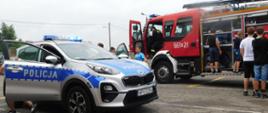 Na zdjęciu widoczne są samochody straży pożarnej i policji oraz dzieci, które z chęcią zwiedzają oba pojazdy.