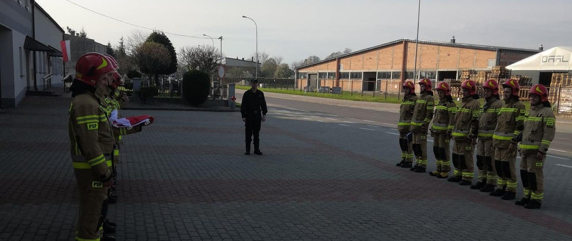 Zdjęcie przedstawia strażaków w ubraniu specjalnym, stojących na zbiórce przed Komendą Powiatową PSP w Lubaczowie