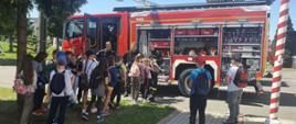 Dzieci i strażacy stoją przy samochodach strażackich. Strażacy opowiadają i pokazują sprzęt. 