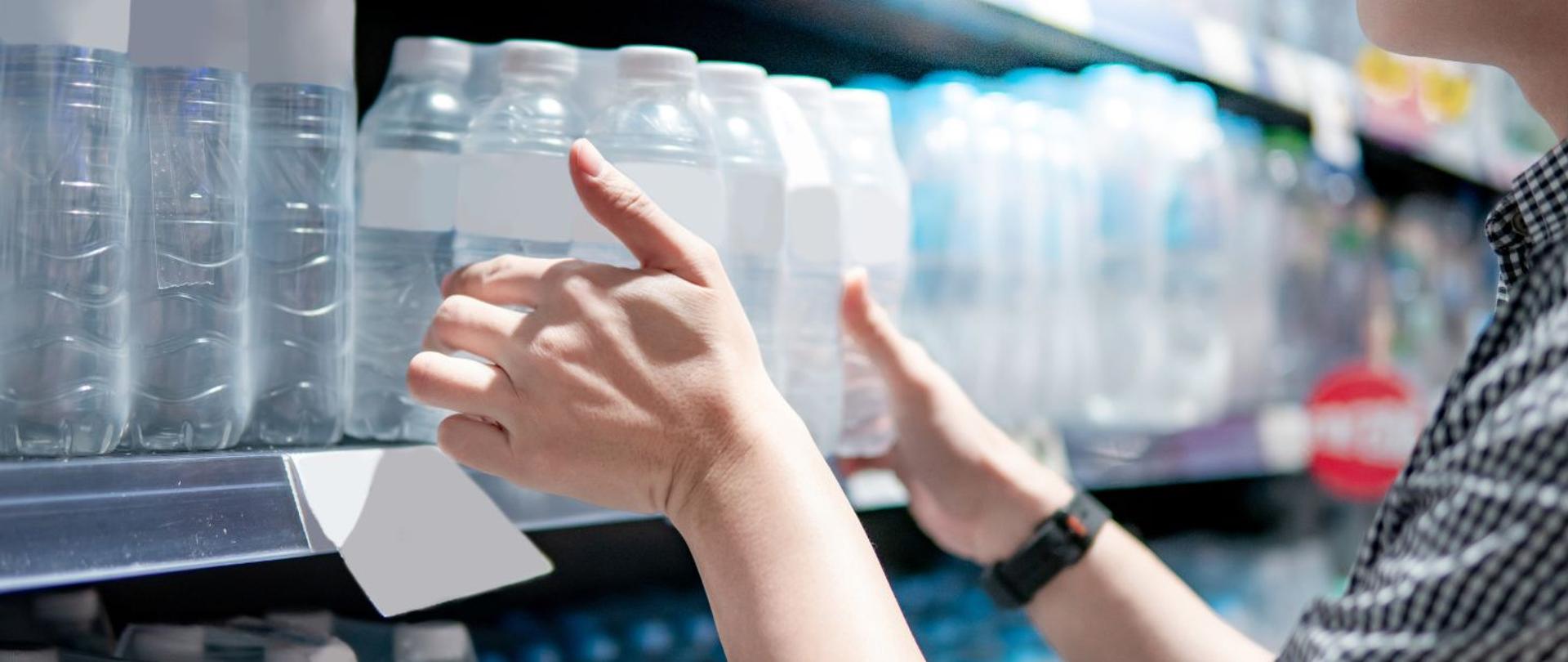 Osoba w sklepie bierze w dłonie sześciopak butelek 