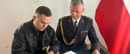 Nowoprzyjęty strazak podpisuje akt ślubowania obok siedzi Komendant Powiatowy