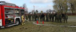 samochód pożarniczy z podpiętą linią wężową oraz leżący sprzęt gaśniczy. Wojska Obrony Terytorialnej obserwują sprawianie sprzętu gaśniczego 