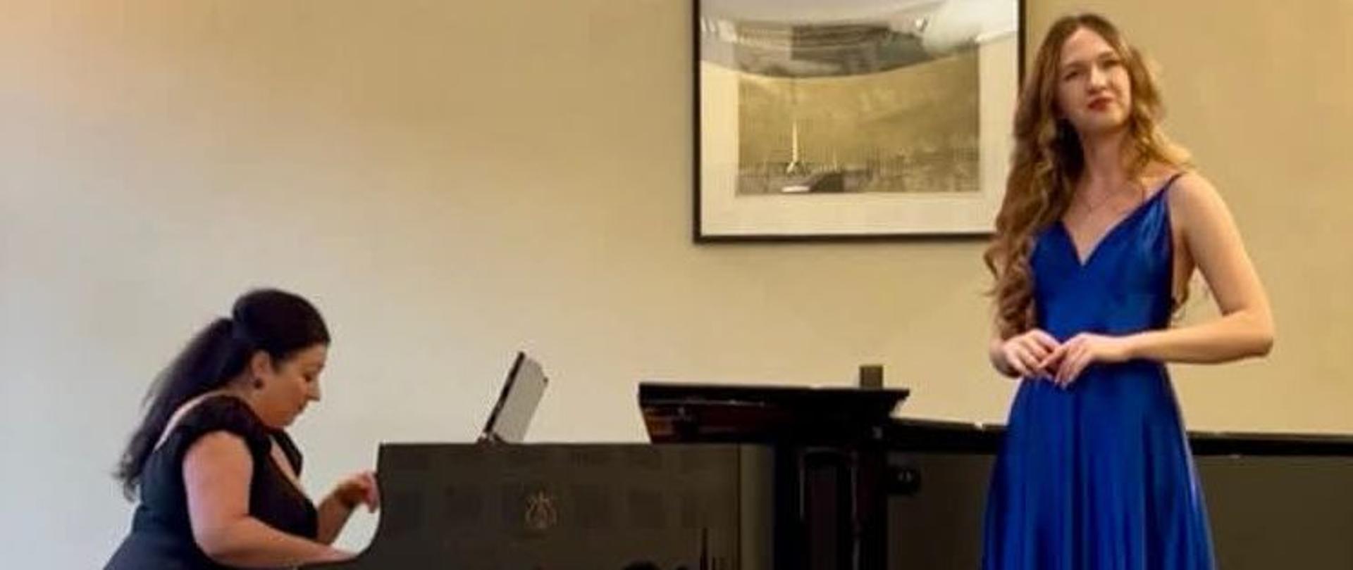 Amelia Szmidt na scenie konkursu w dn. 17.04.2026. Uczennica w niebieskiej sukni, w tle akompaniatorka.