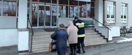 Na zdjęciu dwie kobiety oraz strażak, który jedną z nich trzyma pod rękę. Cała trójka stoi przed schodami przed lecznicą.