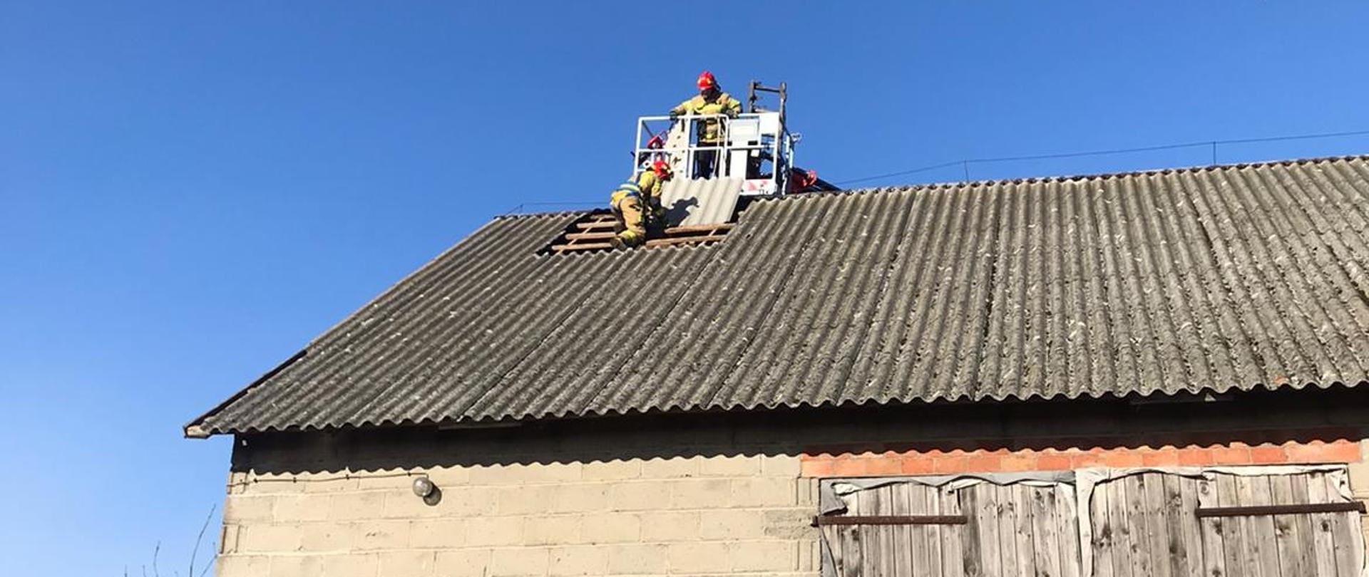 Trzej strażacy na dachy budynku gospodarczego szykują się do zakrycia dziury w dachu , w którym wiatr wyrwał kilka płyt eternitu