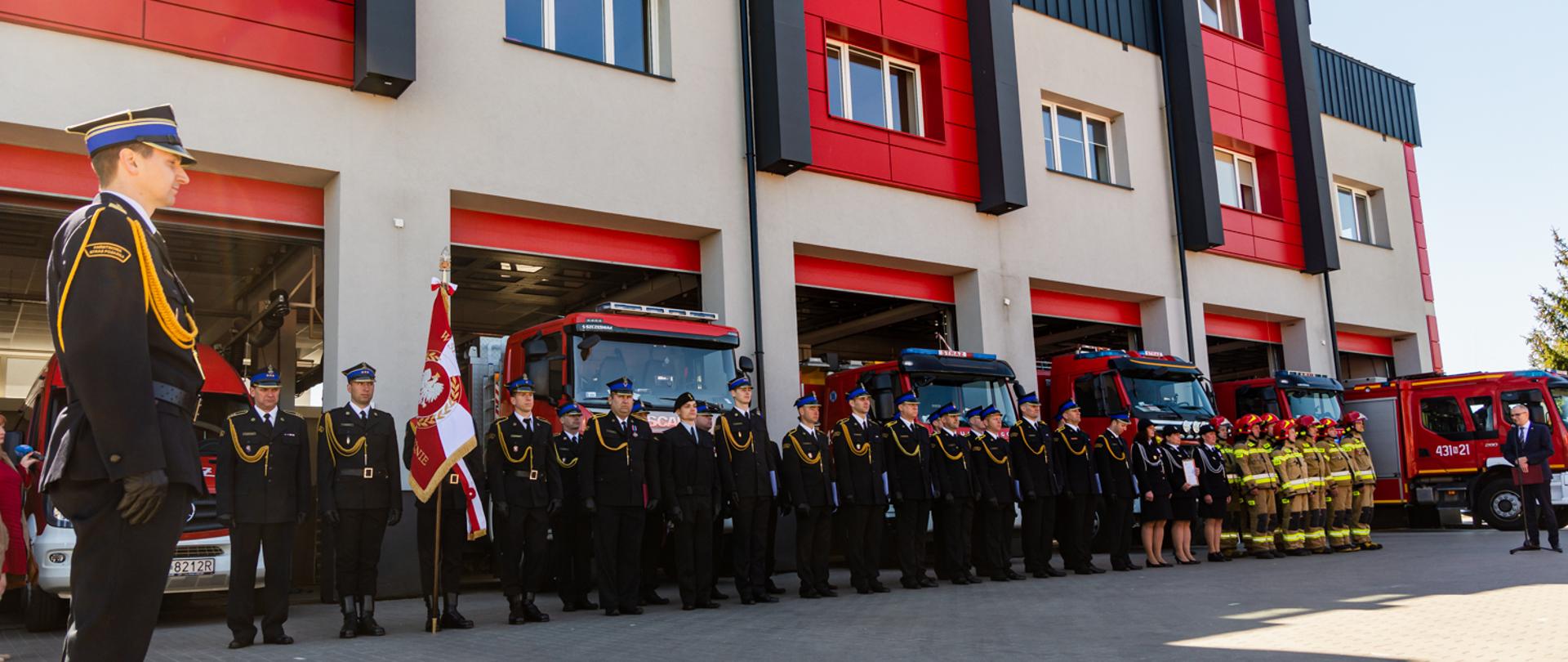 Zdjęcie przedstawia poczet sztandarowy oraz pododdział KP PSP w Ełku składający się ze strażaków w umundurowaniu galowym oraz ubraniach specjalnych.