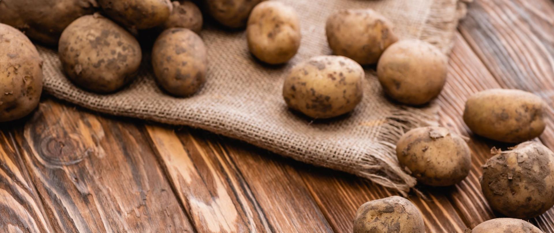 Na zdjęciu są ziemniaki. Leżą na drewnianym blacie.