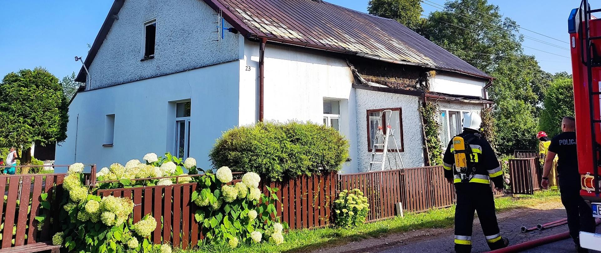 Zdjęcie przedstawia strażaków pracujących podczas gaszenia domu widać budynek węże samochód strażacki strażaków