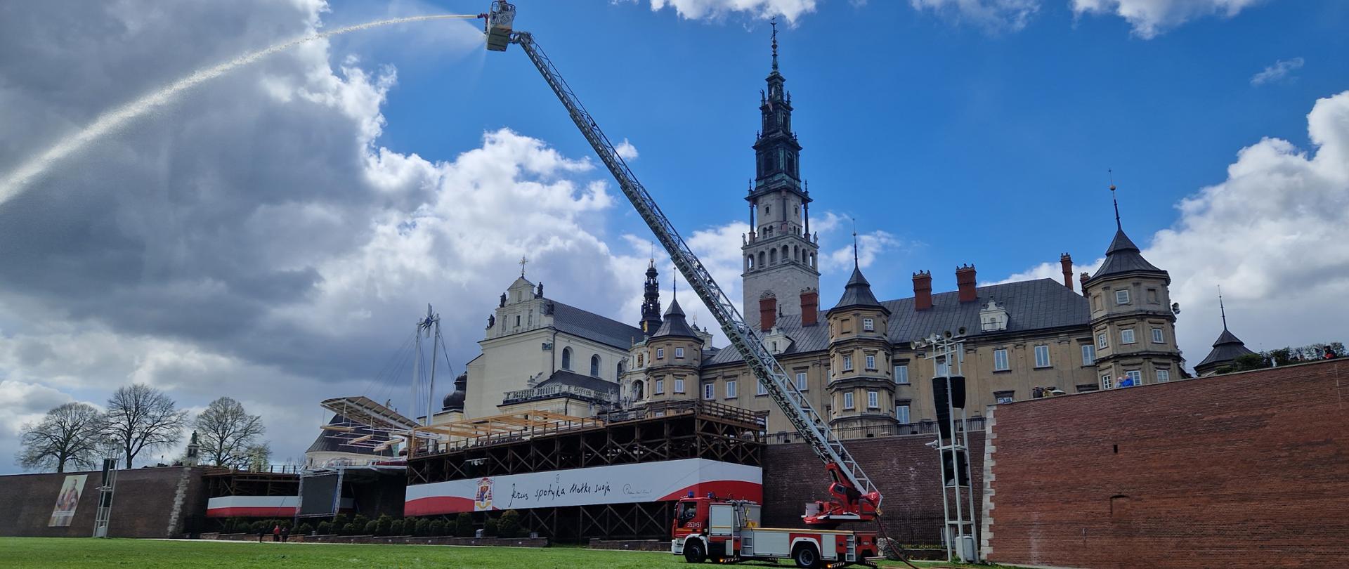 Zdjęcie przedstawia samochód z drabiną mechaniczną rozłożony na Błoniach Jasnogórskich strażak w koszu na górze podaje prąd wody z działka wodnego