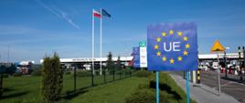 Przejście graniczne z Unią Europejską. Baner Unii Europejskiej, w tle flagi Polski i Unii Europejskiej, przejazd na samochody.