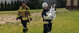 Na zdjęciu dwóch strażaków, jeden z nich zwija wąż pożarniczy