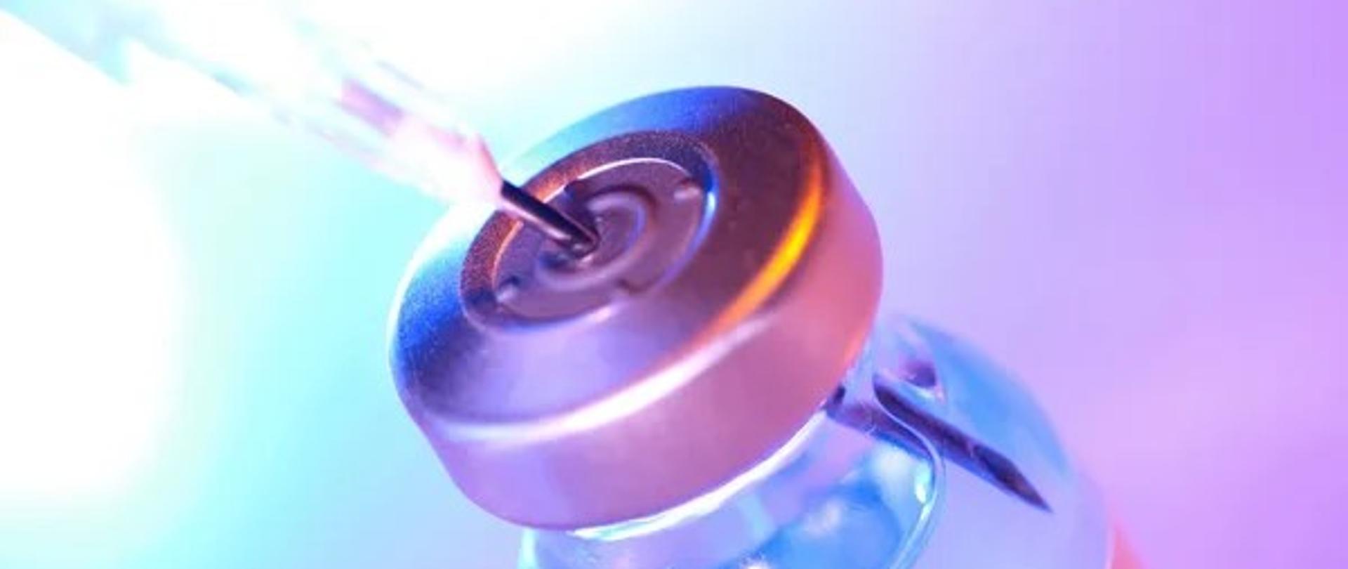 Fiolka ze szczepionką z wpitą strzykawką na niebiesko-fioletowym tle.