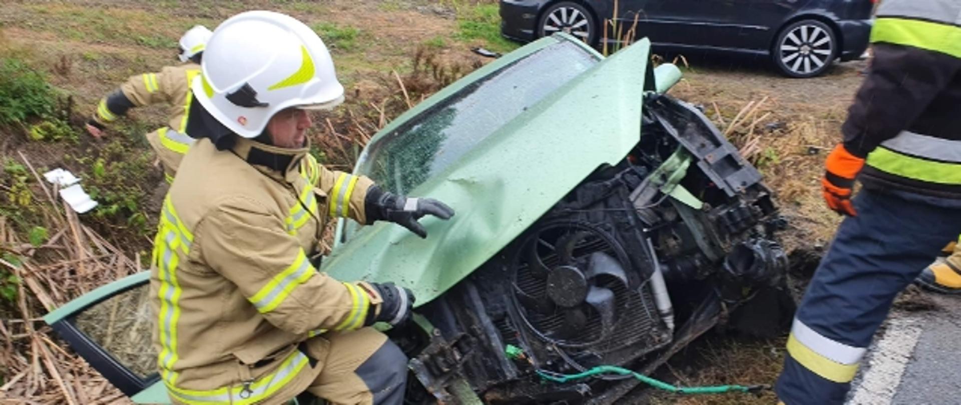 Zniszczony samochód w rowie a obok niego strażacy.
