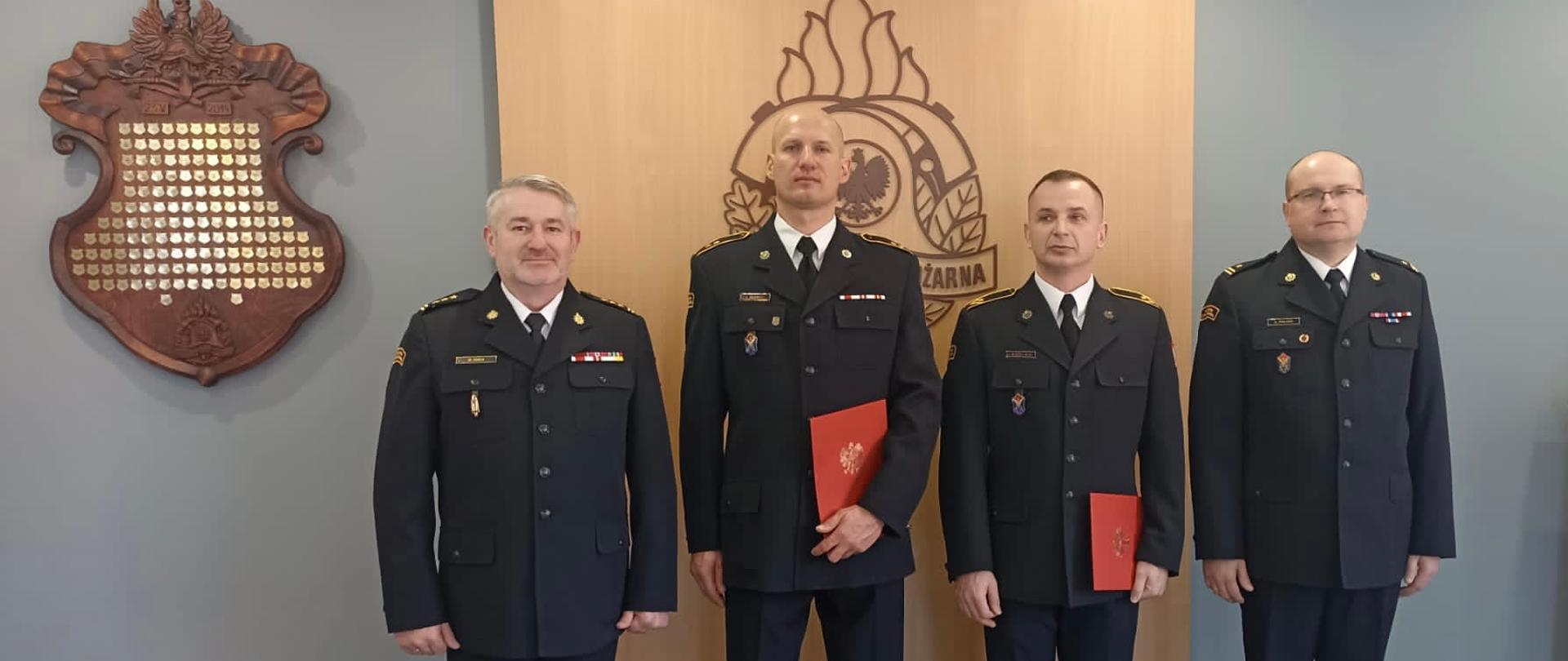 wspólne zdjęcie komendantów z awansowanymi strażakami na tle loga psp