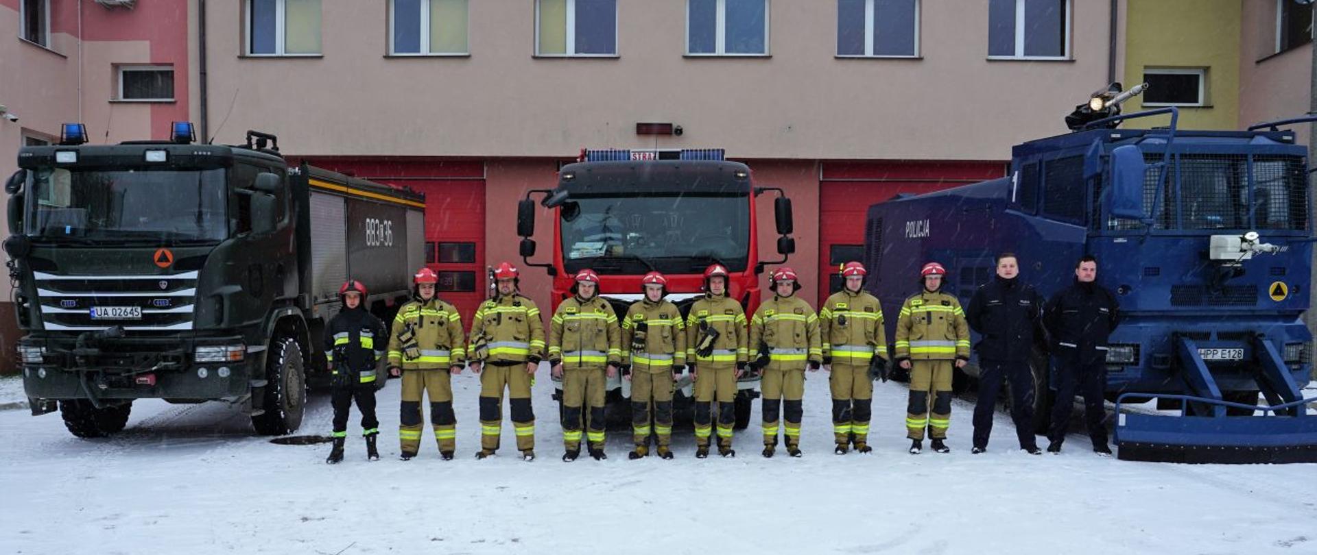 Widoczna policja strażacy na tle garażów jrg Hajnówka, widoczne pojazdy straży wsp i policji