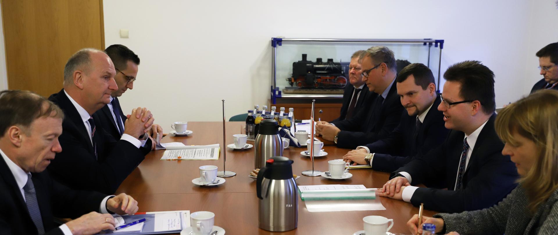 Na zdjęciu widać grupę ludzi którzy siedzą przy stole. W tle widać figurę lokomotywy kolejowej. 